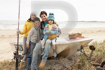 Family Group Sitting On Boat With Fishing Rod On Winter Beach