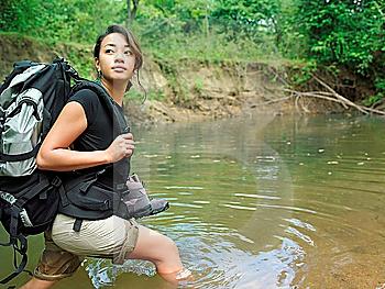 Young woman carrying backpack walking in water looking over shoulder