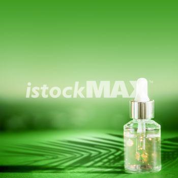 Cosmetic bottle with pipette standing on green table with palm leaves shadow. Facial skin care concept. Natural vegan cosmetic. Serum or skin essential oil. Modern beauty trend.