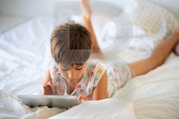 Little girl, eight years old, playing with digital tablet on the bed.. Little girl playing with digital tablet on the bed.