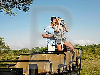 Couple on safari standing in jeep woman looking through binoculars