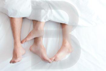Closeup feet of couple on the bed. Man and woman lovers make love under the blanket or bed sheet. Sex on vacation theme. Valentine and Honeymoon concept.