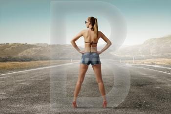 Hitch hiker woman on road. Young attractive girl in bikini and shorts on road