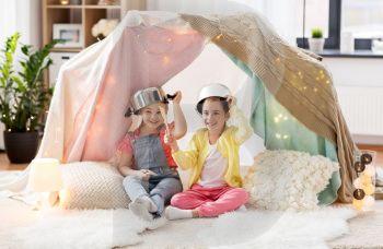childhood and hygge concept - happy little girls with cooking pots playing in kids tent at home. girls with kitchenware playing in tent at home. girls with kitchenware playing in tent at home
