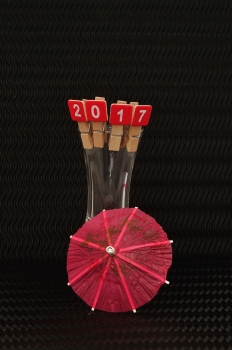 2017 spelled with red blocks displayed with a shooter glass with a red cocktail umbrella on a black background