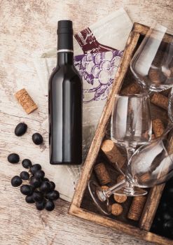 Bottle of red wine and empty glass with dark grapes with corks and opener inside vintage wooden box on wooden background with linen towel. Macro