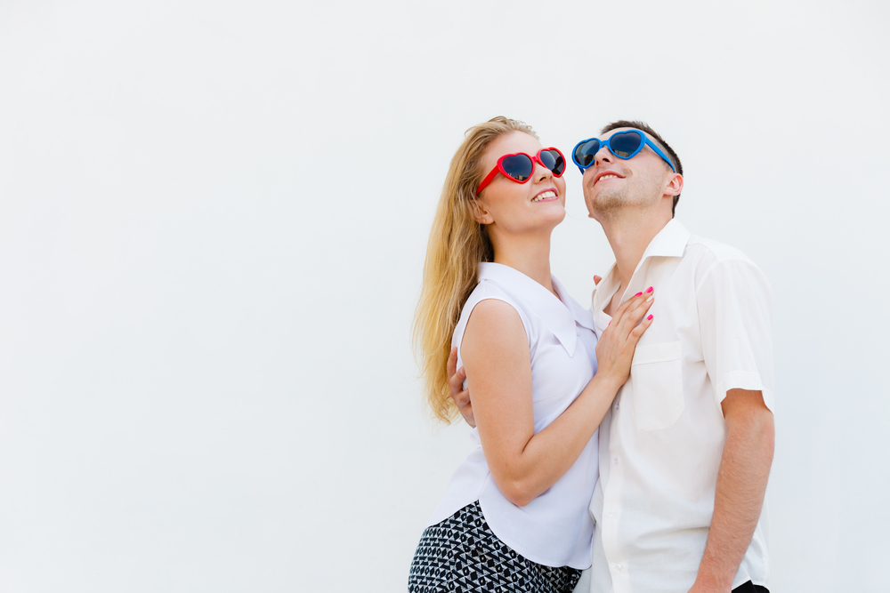 Love, relationship goals, funny accessories concept. Man and woman wearing heart shape sunglasses looking happy.. Man and woman wearing heart shape sunglasses
