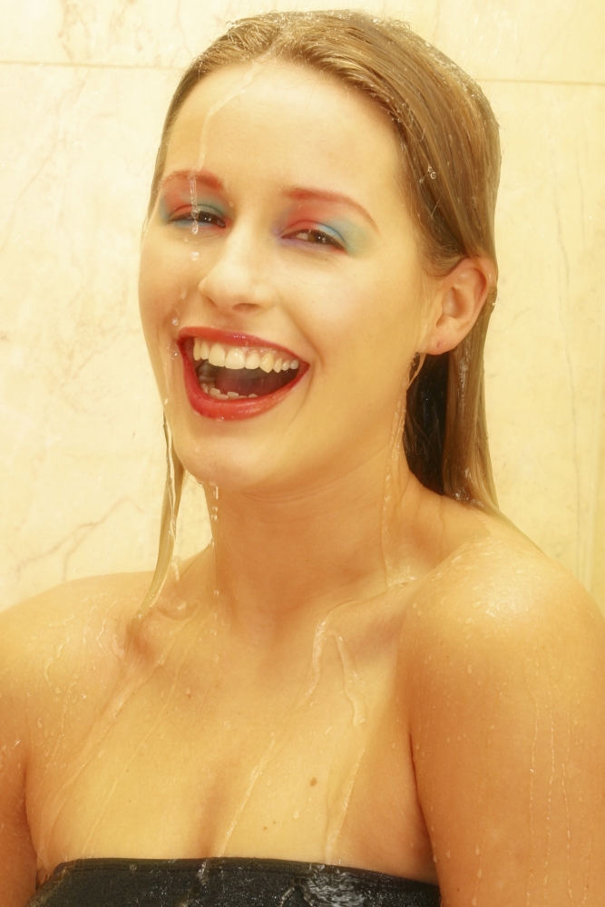 20s woman in shower with water flowing over her face looking at the camera happy and laughing.