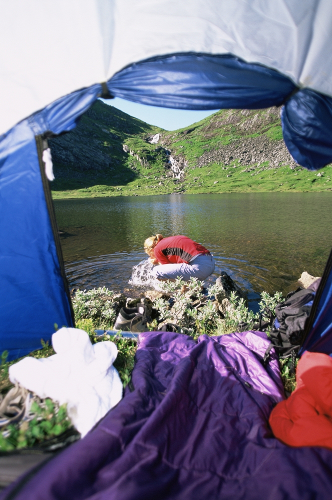 Woman outdoors at campsite by tent splashing water from river on face