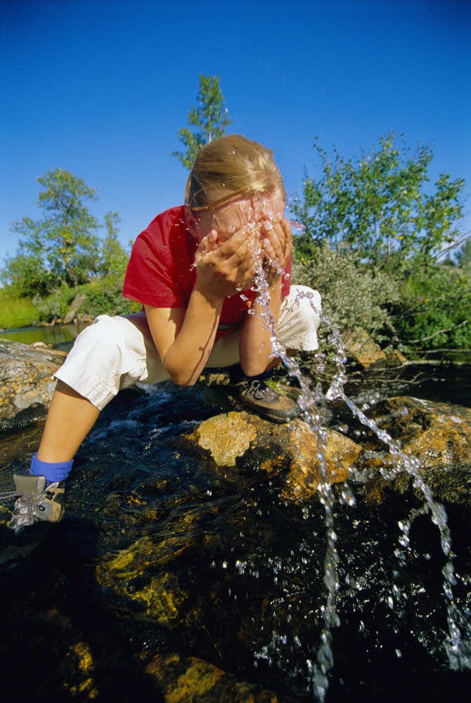 Woman outdoors by a lake splashing water on face