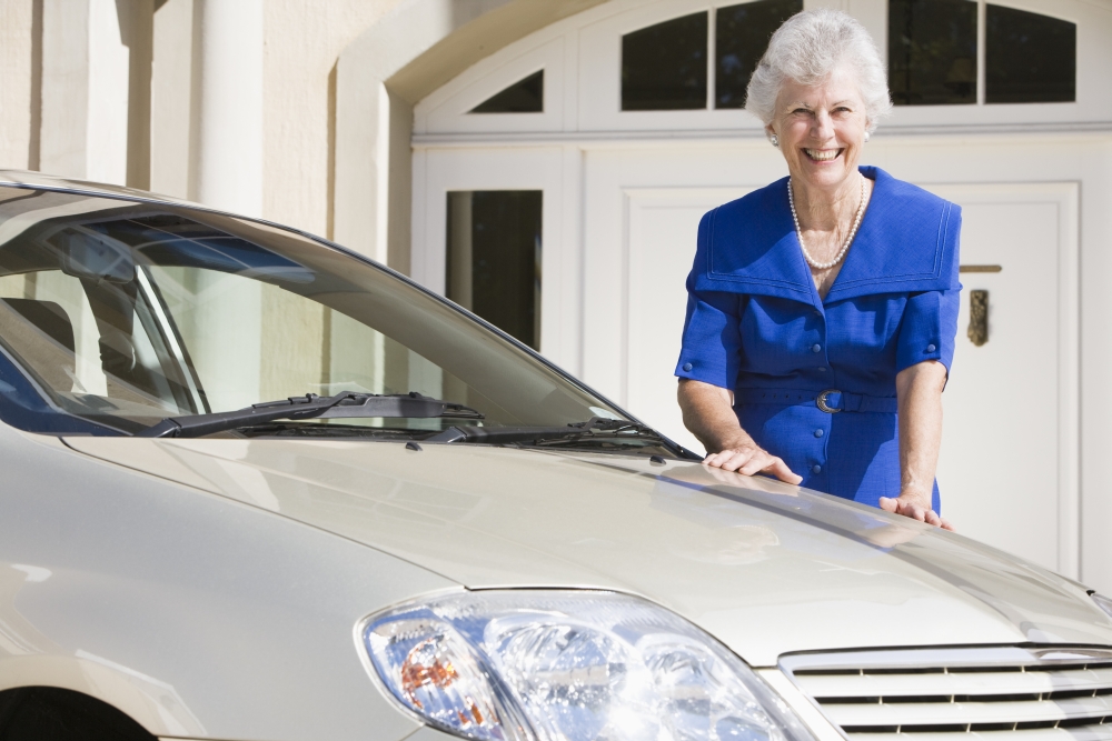 Senior woman standing with her car outside her home