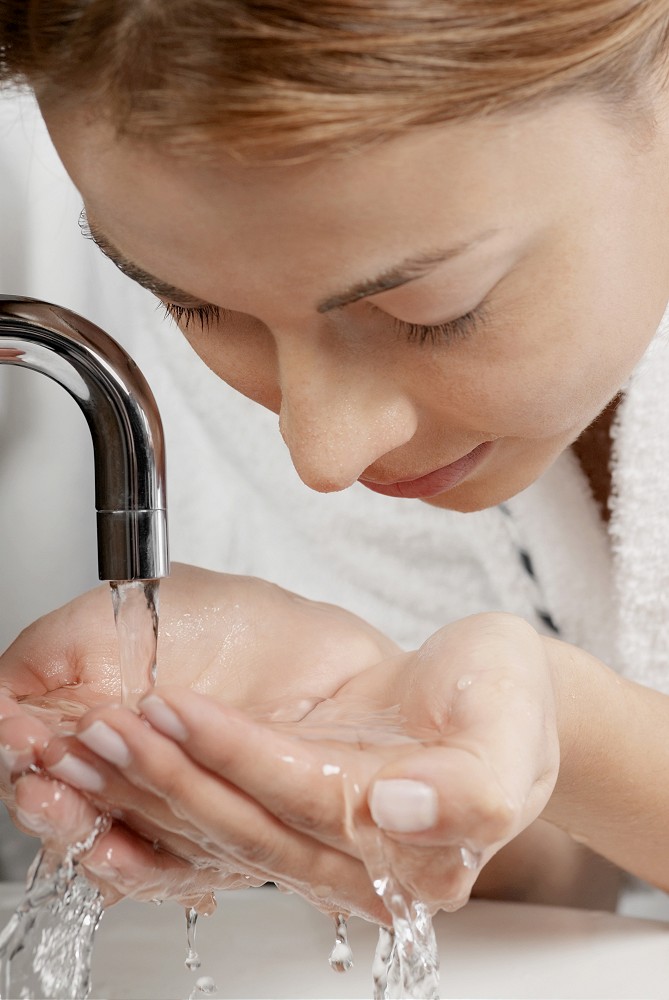 Close-up of a young woman washing her face in the bathroom sink