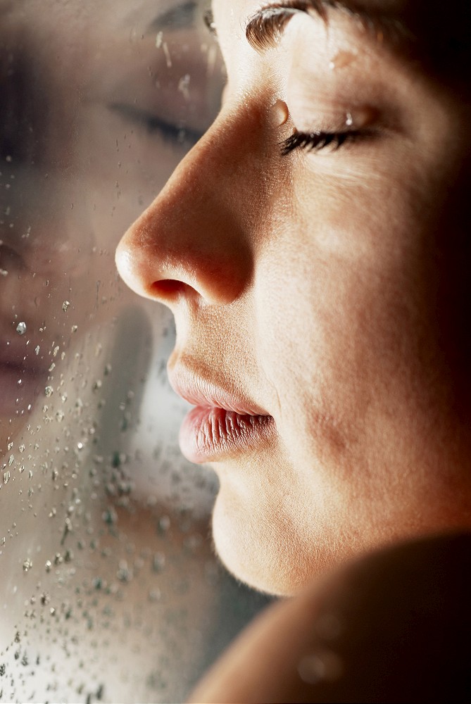 Close-up of a young woman with her face against a glass window