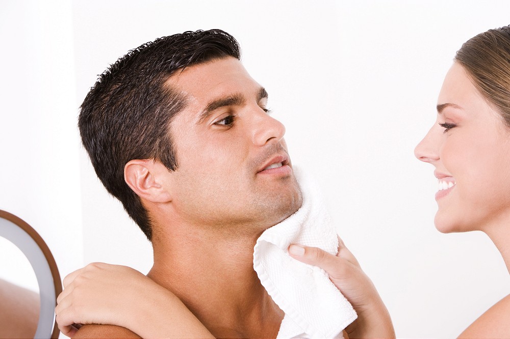 Close-up of a young woman wiping a mid adult man&acute;s face with a towel
