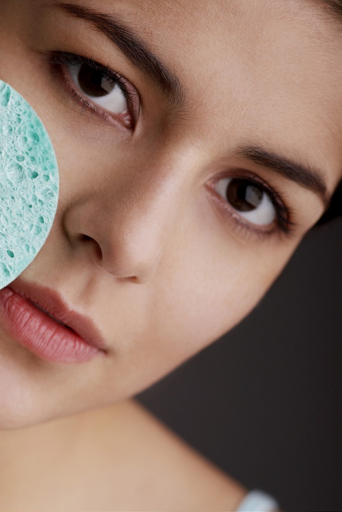Portrait of a young woman scrubbing her face with a sponge