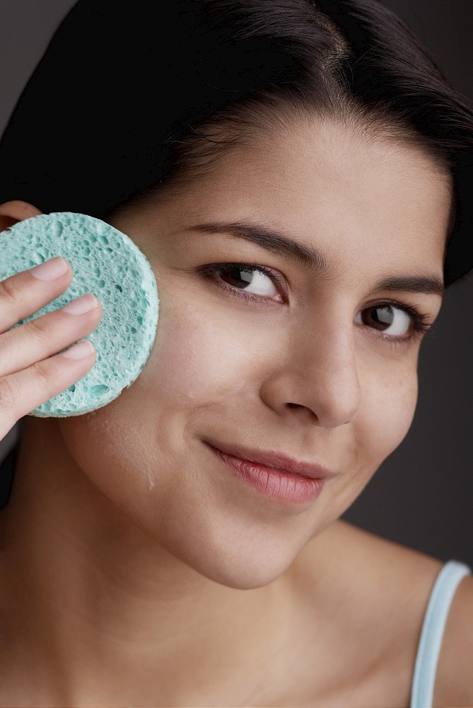 Portrait of a young woman scrubbing her face with a sponge