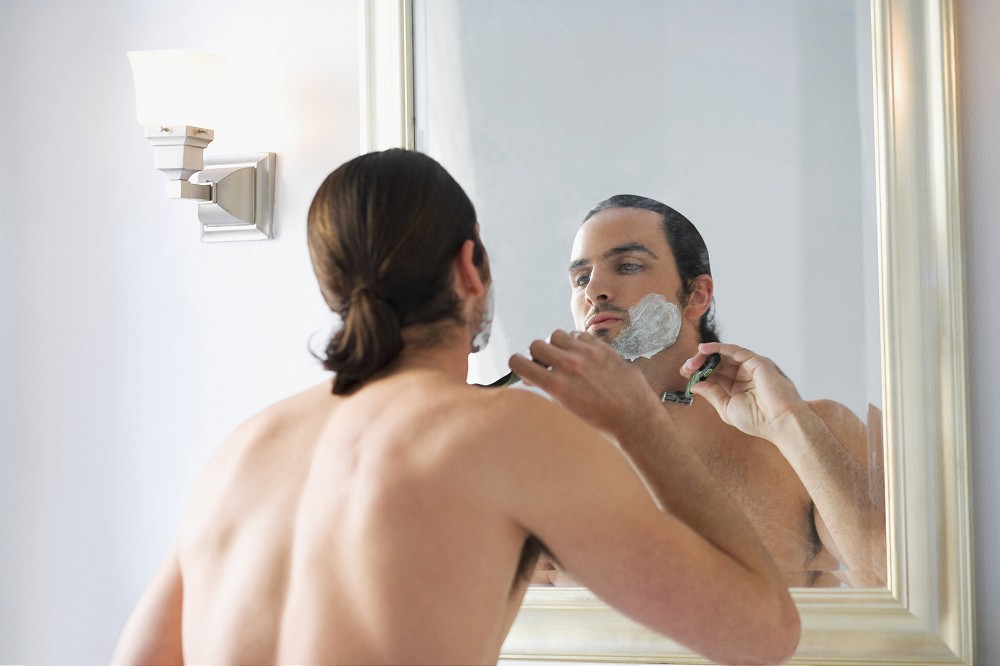 Rear view of a young man shaving his face