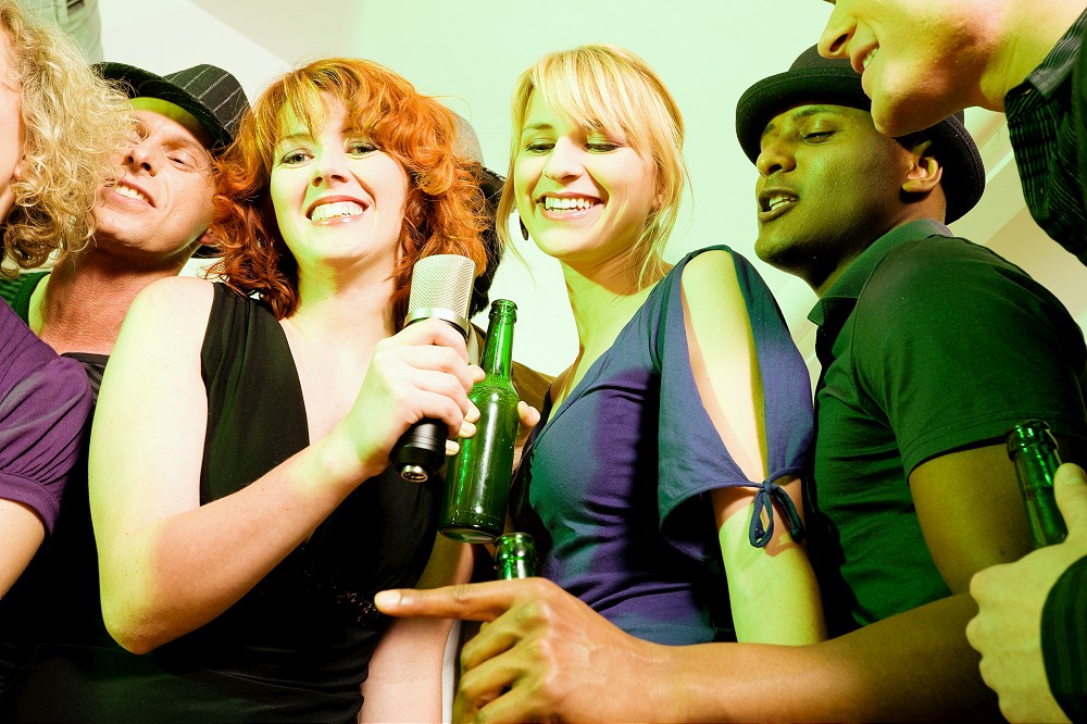 Group of friends (diversity) at a party in a club doing karaoke and drinking beer