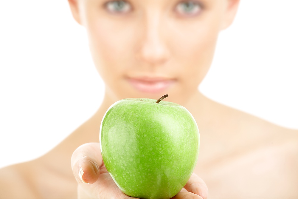 Close up of a green apple against a woman&acute;s face, isolated