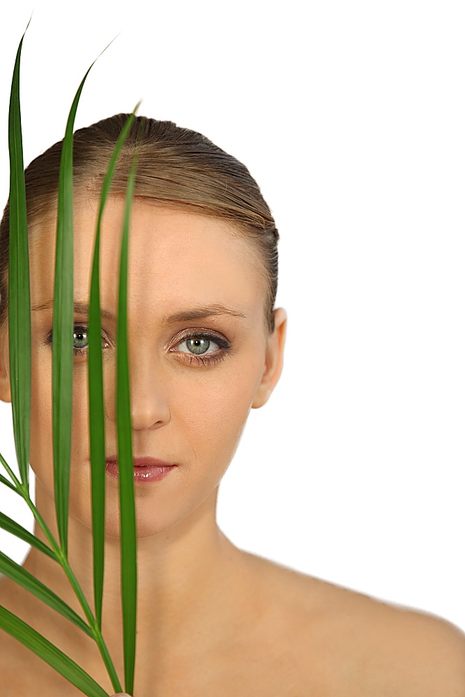 Woman in makeup holding a leaf in front of her face