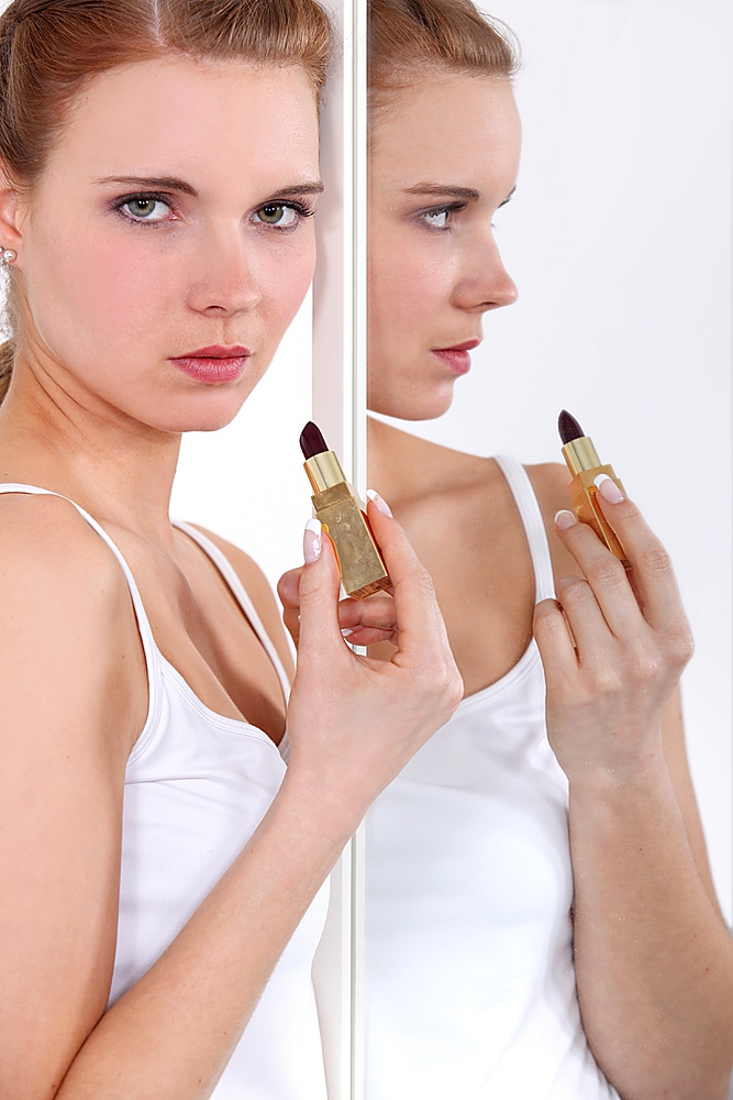 Young woman applying lipstick in a mirror