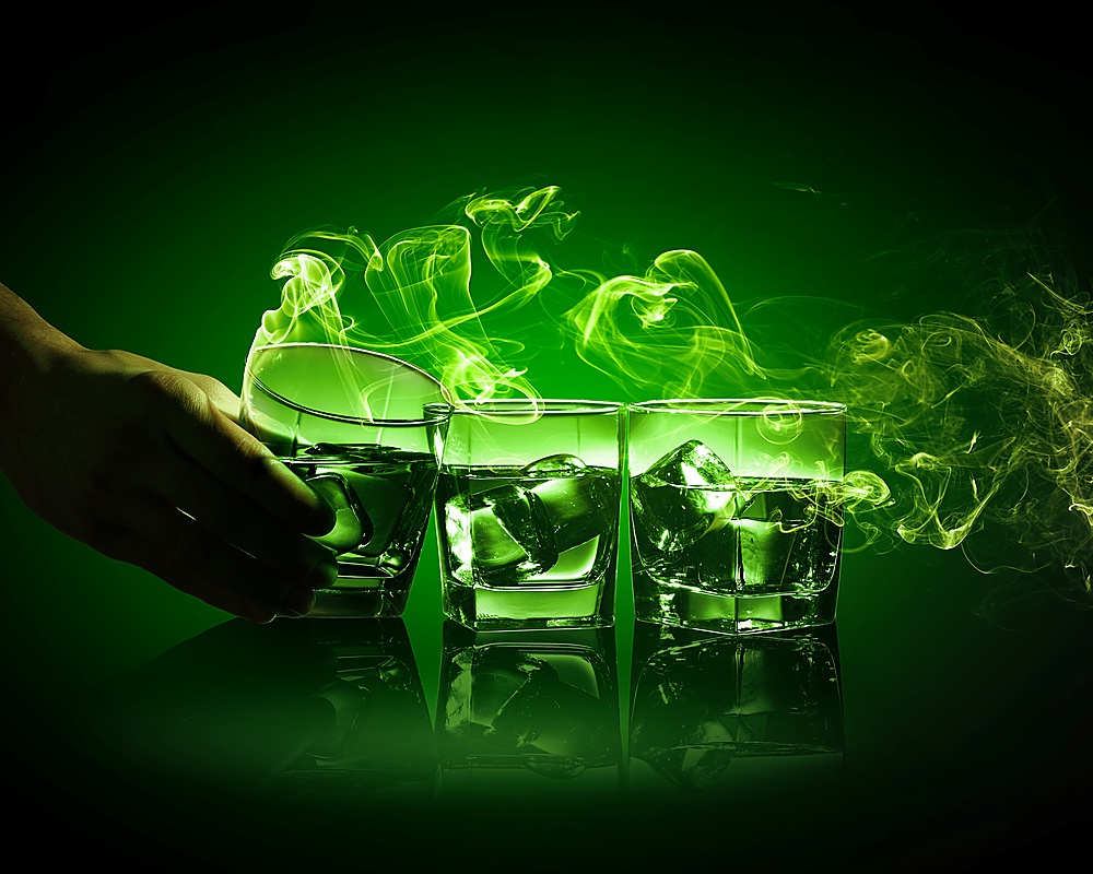 Hand holding one of three glasses of green absinth with fume going out