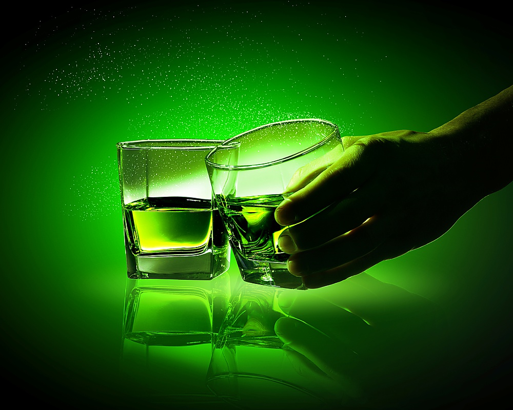 Hand holding one of two glasses of green absinth