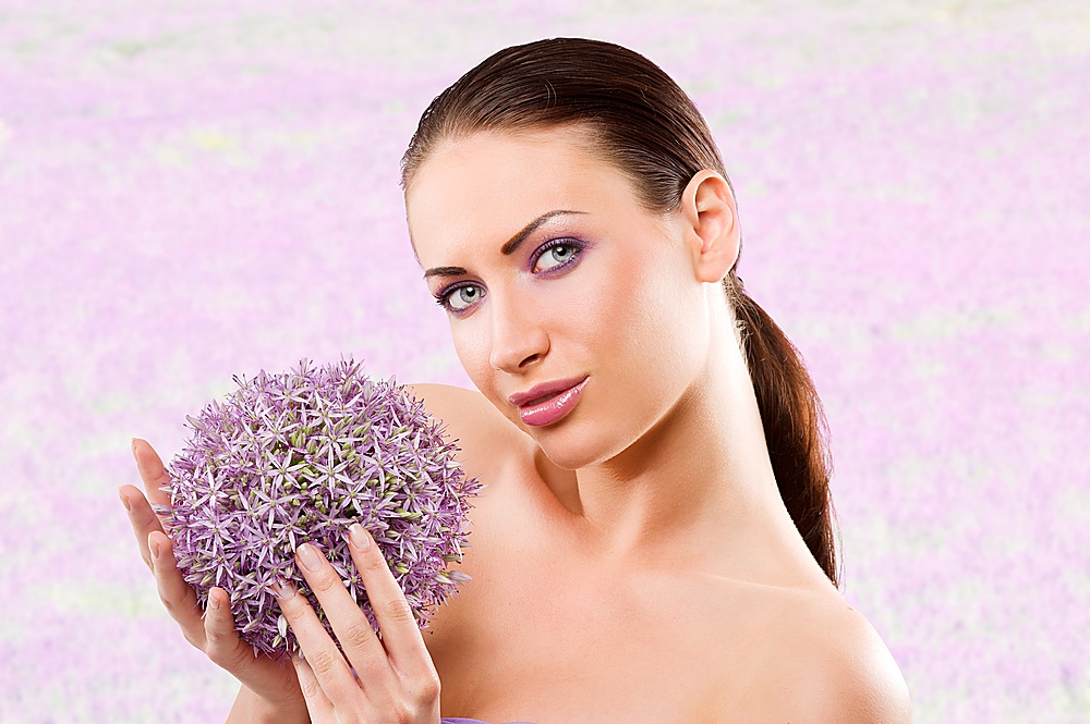 young and beautiful brunette woman in a beauty portrait with some purple flower near face
