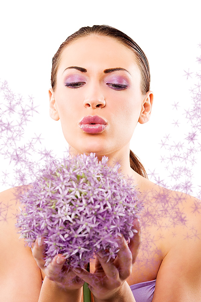 young and beautiful brunette woman in a beauty portrait blowing on purple flower