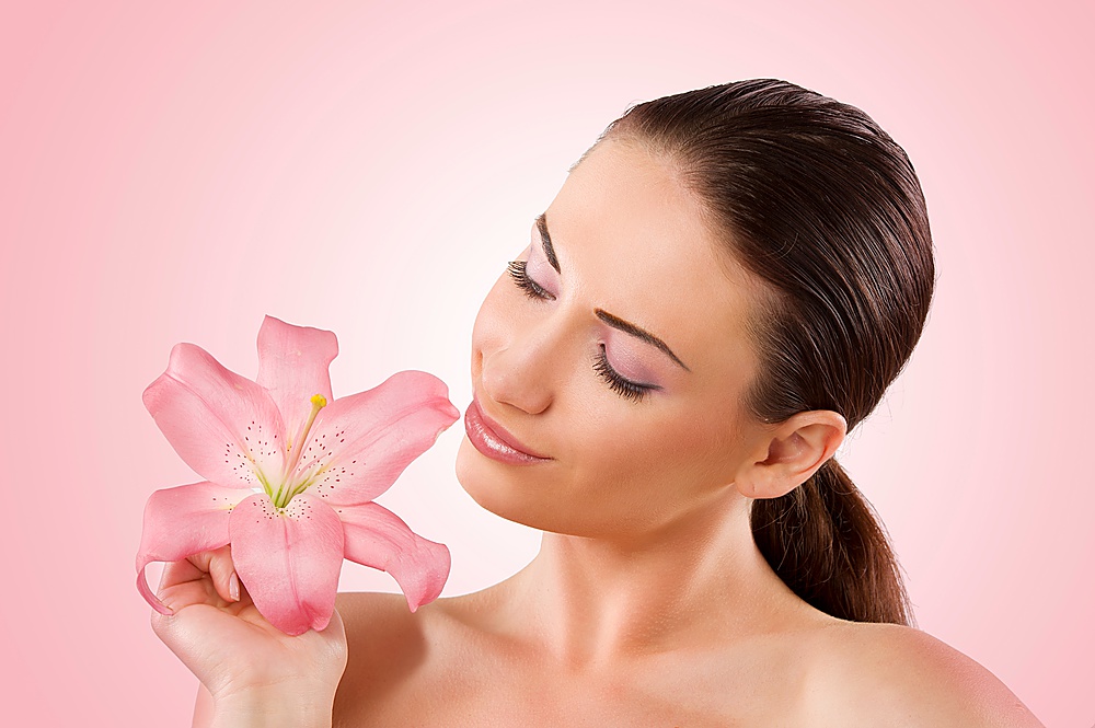 Fresh portrait of a pretty young woman looking at a pink lily