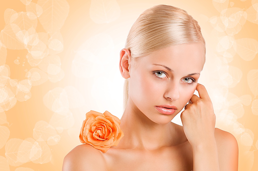 beauty portrait af sweet and nice blond girl with an orange rose on her shoulder looking in camera