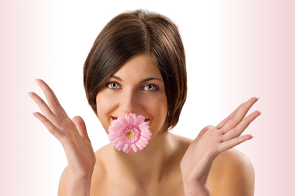 very nice and sweet girl in a funny shot looking in camera and keeping a pink flower in mouth