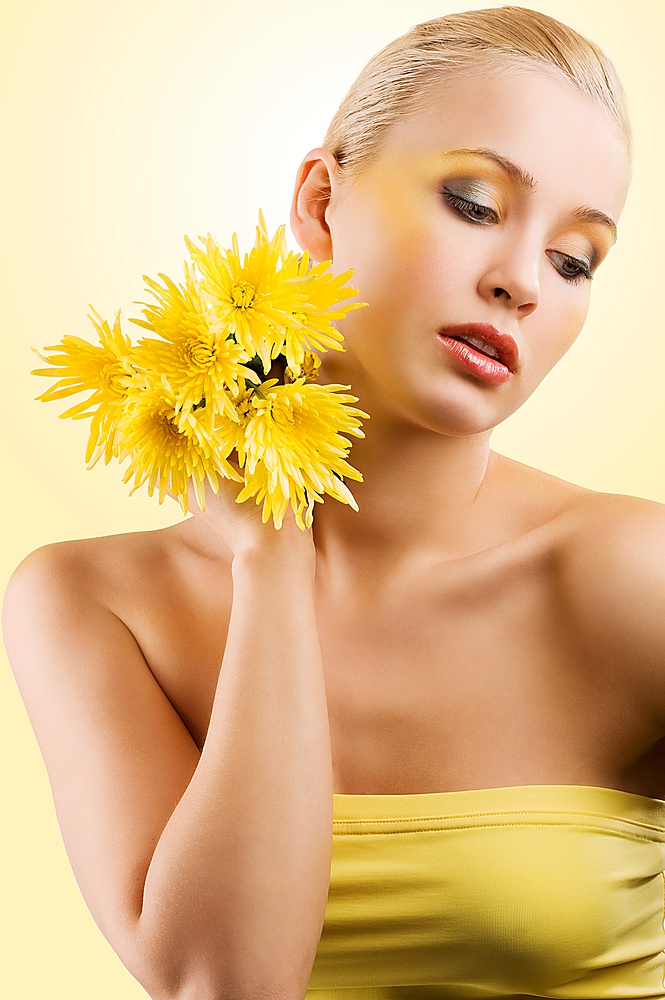 sweet and beauty blond girl wearing a yellow top keeping yellow flower and looking down. wellness concept