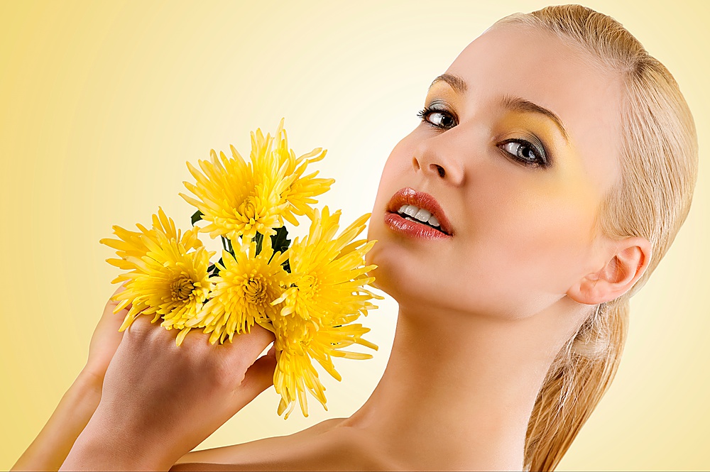 close up portrait of young and beauty blond girl keeping yellow flower and smiling. wellness concept