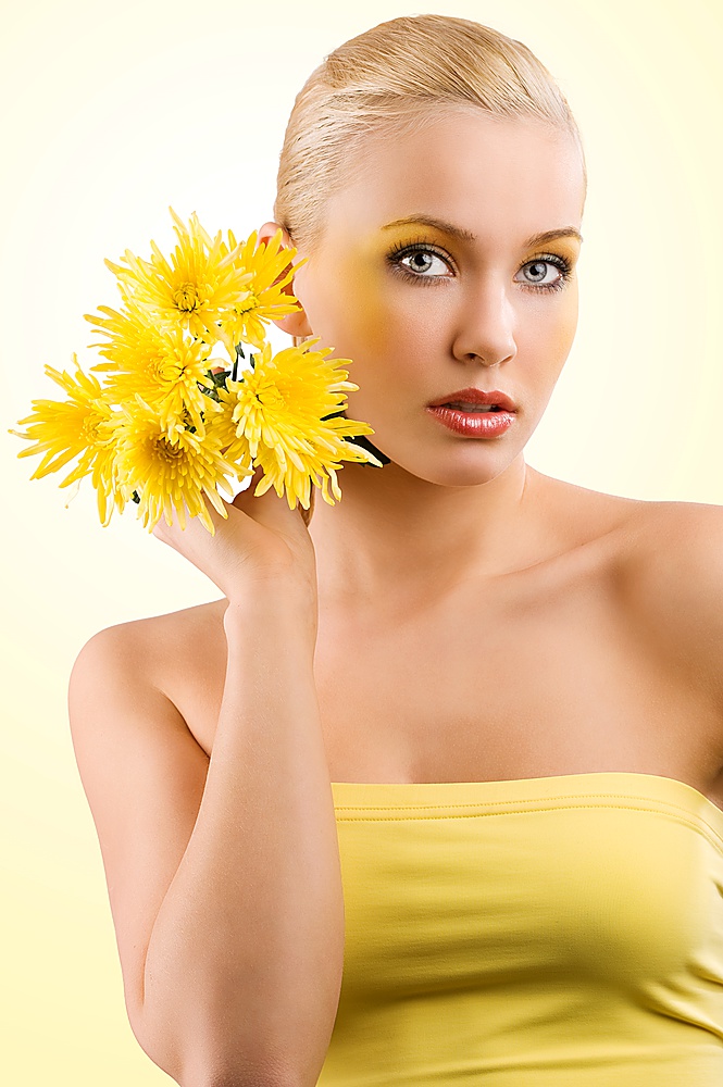 young and beauty blond girl wearing a yellow top keeping yellow flower. wellness concept