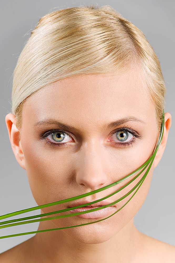 beauty shot of a blond girl with some blade of grass around her face. wellness concept