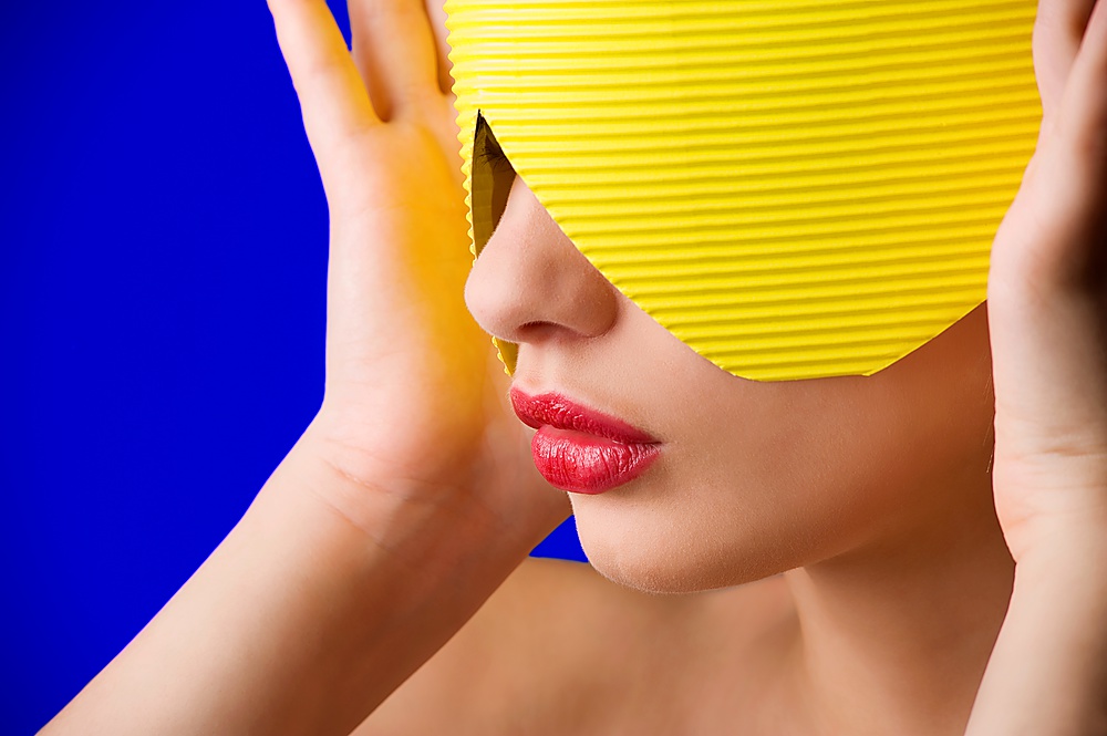 beauty portrait of a young woman with a yellow paper mask and red lips on blue background