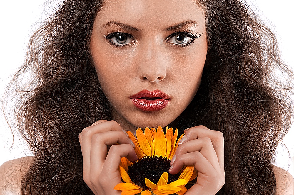beauty portrait of a fresh and natural girl with long curly hair holding a sunflower