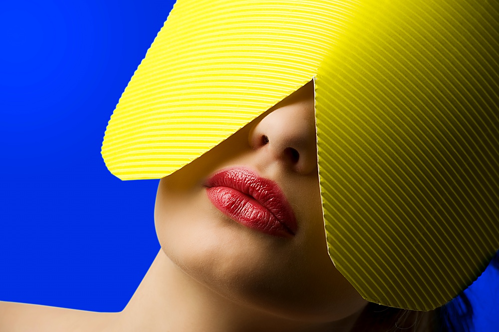 close up portrait of a young woman with a yellow paper mask and red lips on blue background