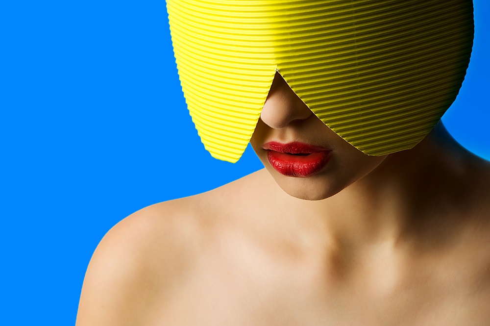 fashion portrait of a young woman with a yellow paper mask and red lips on blue background