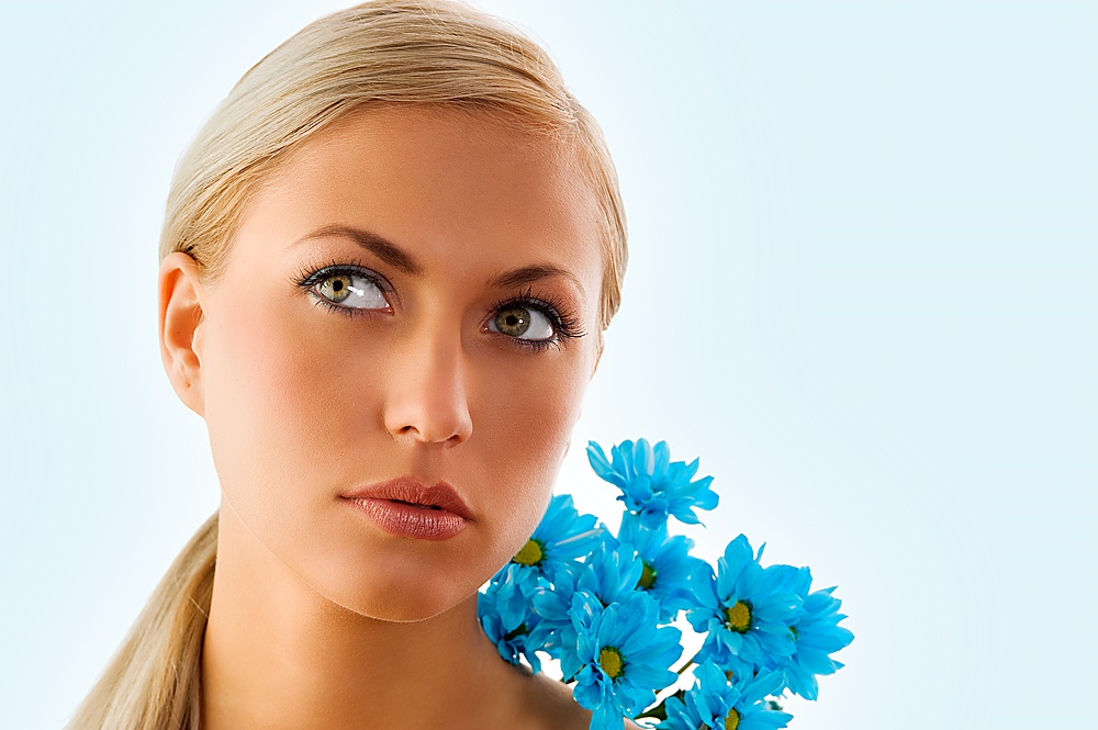 pretty blond girl in a beauty portrait with blue daisy on her shoulder