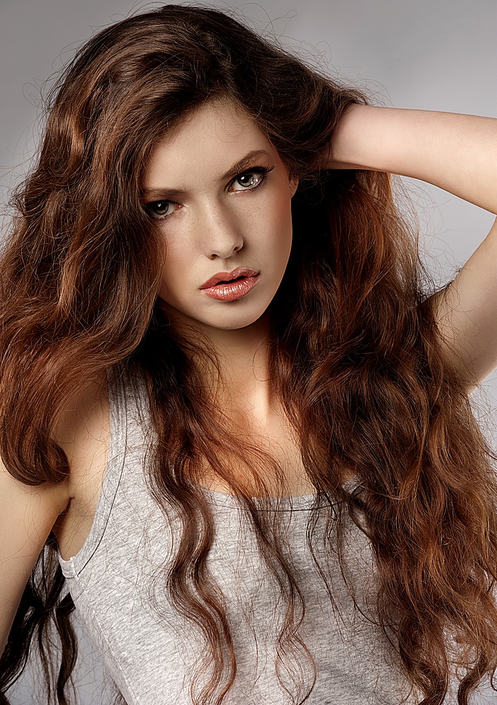 very nice and fresh young girl with long curly hair in a fashion portrait looking in camera