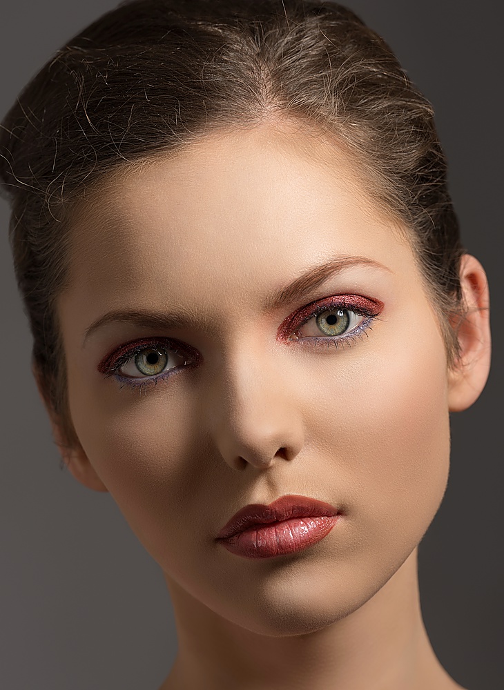 close-up portrait of beauty girl with green eyes, red glossy make-up and brown hair on gray background