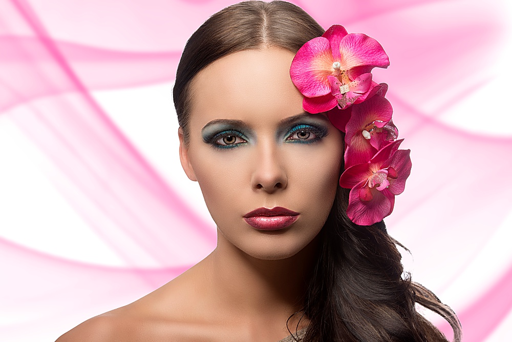 beauty portrait of brunette with coloured make-up and pink flower. FLOWERS ARE FAKE