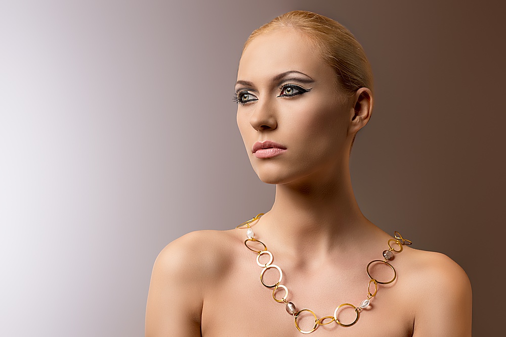 very beauty blonde woman with elegant make-up wearing gold ringed necklace on nude shoulders