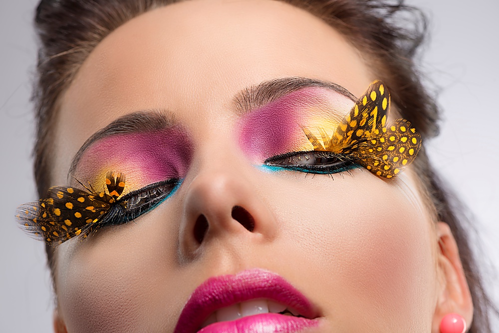 beauty close-up portrait with colored and feathered make up, she looks down at left