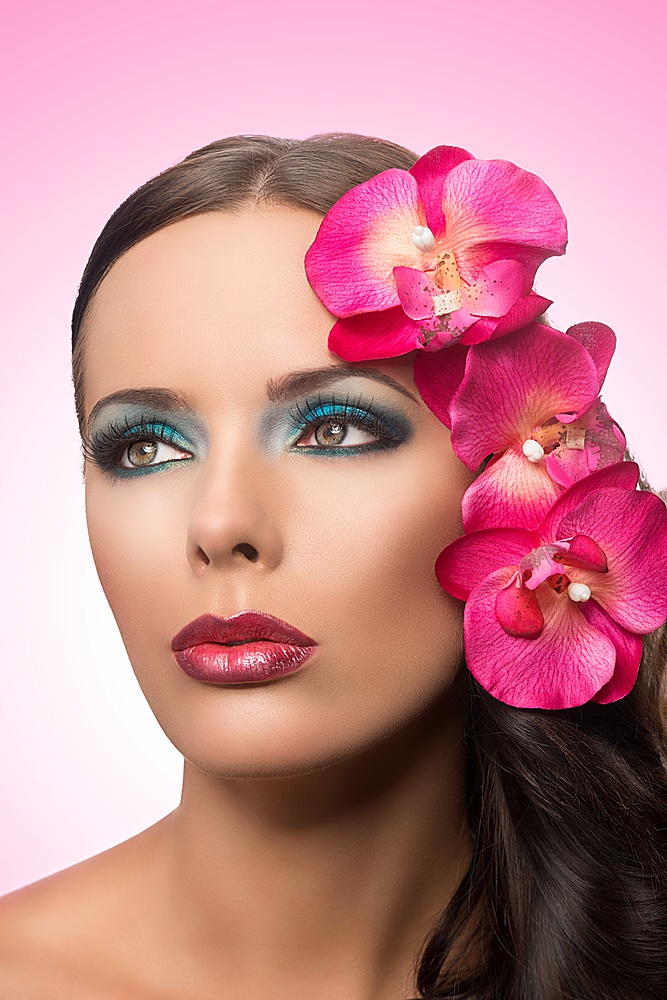 beauty portrait of brunette with coloured make-up and pink flowers . flower are fake