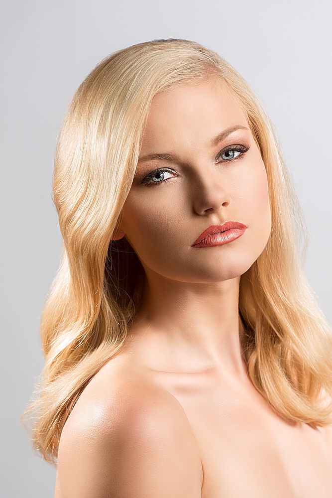 beautiful blonde girl with smooth hair and naked shoulders, her body is turned of three quarters at left and she looks in to the lens