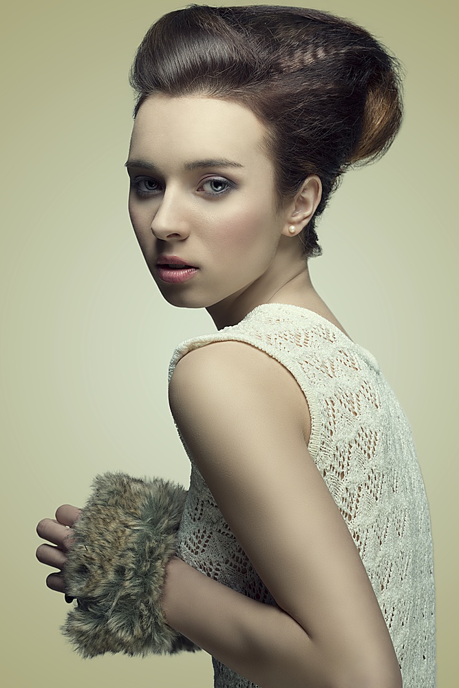 beautiful young girl with brown fashion hairdo looking in camera and taking in the hand fur accessory