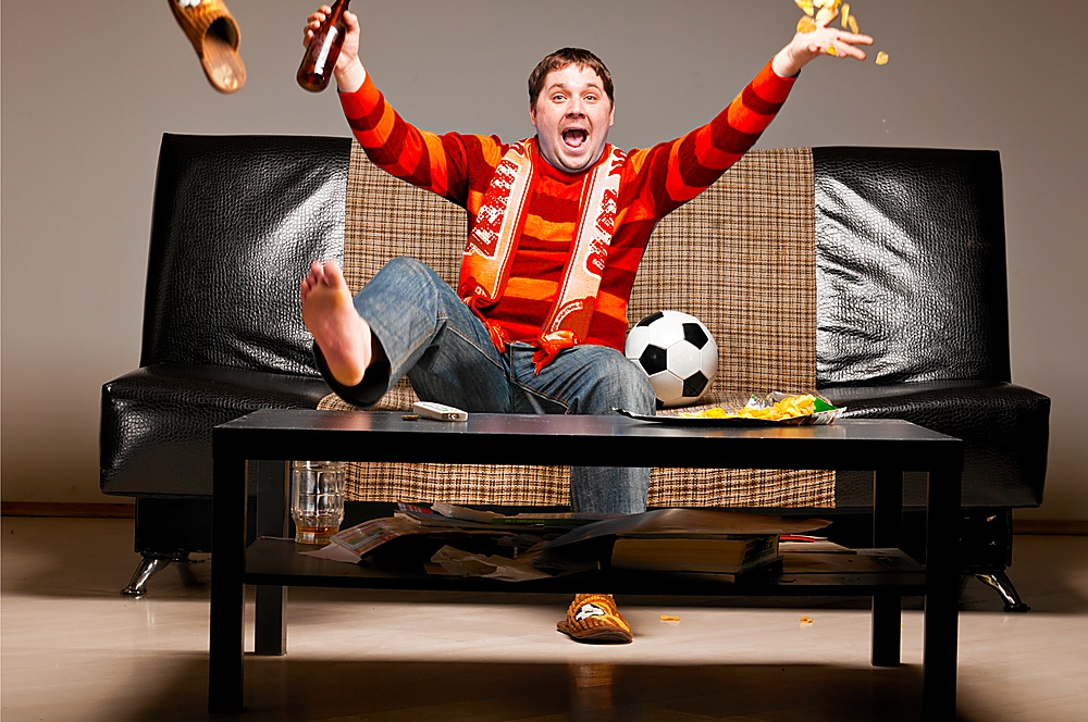 soccer supporter is sitting on sofa in red jersey